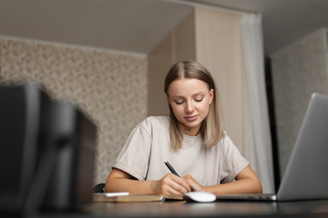 A cute pensive girl smiles and does work from home; takes notes in a notebook during quarantine and a pandemic. plan full face