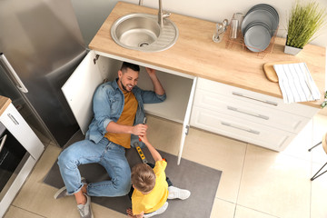 Little son helping his father to repair sink in kitchen