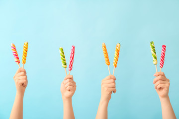 Hands with sweet lollipops on color background