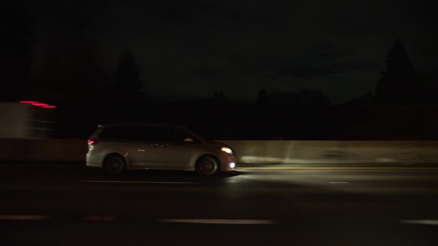 A silver minivan overtakes on a freeway at night