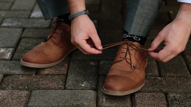 Slide shot of a groom tying his brown leather shoes on his wedding day