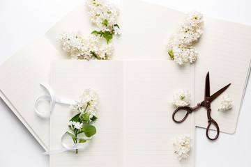 Notebooks, beautiful lilac flowers and scissors on white background