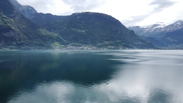 drone flight over a beautiful swiss lake (Urnersee) with green forest, white mountains and clouds