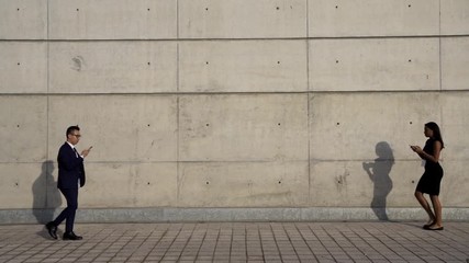 Full length view,busy multicultural business people in formal wear strolling and using modern smartphones during walk in urban setting.Diverse business people with mobile phones in hands hurry to work