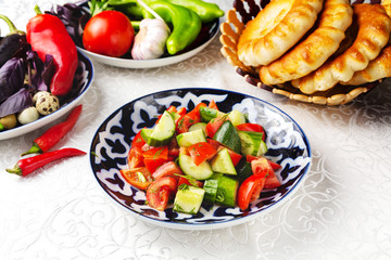 Salad of fresh vegetables, tomatoes, cucumbers, greens. Traditional oriental dish. On a plate on a table in a restaurant.