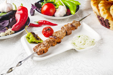 Meat skewers, beef skewers, lamb skewers, oriental lunch, fresh vegetables. On a plate on a table in a restaurant.
