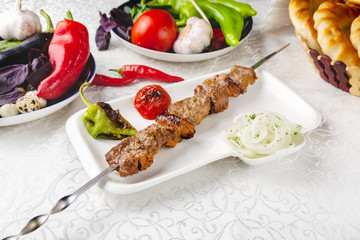 Meat skewers, beef skewers, lamb skewers, oriental lunch, fresh vegetables. On a plate on a table in a restaurant.
