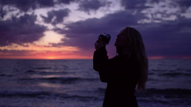 Silhouette of Woman Photographer Taking Photos with Dramatic Ocean Sunset and Cloudscape Background