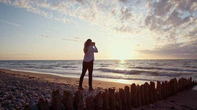 Woman Taking Photos of Beautiful Beach Sunset, Slow Motion Waves Rolling into Shore with Stunning Cloudscape