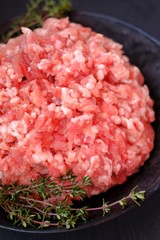 forcemeat with sprigs of thyme in a black cup on a black  background.Meat food. Ground chopped meat and spicy herbs.Minced pork.Protein food.Texture of fresh cut forcemeat 