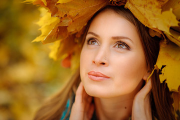 Close up portrait of a beautiful girl in a dark vest. On the head is a lush wreath with autumn leaves. The girl looks away.