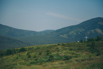 Naklejka premium green mountains and a cross on the horizon. religious object to nature. Church building, ritual symbol, cemetery