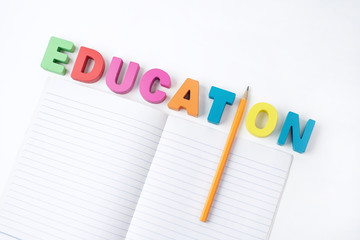 Multicolored Wooden Letters " EDUCATION " with Orange Pencil Instead ' I ' Letter and Paper Book on White Background, Learning English                                                             