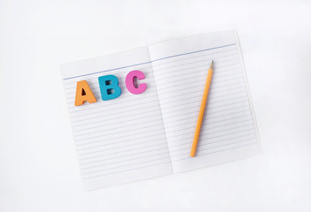 A B C wooden letters alphabet on a paper book with orange pencil on white background
