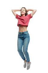 Smiling happy young girl in jeans emotionally jumping while holding hands behind her head. Isolated on a white background. Full height. Vertical.