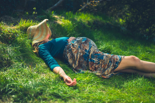 Pregnant woman with hat relaxing on grass in spring