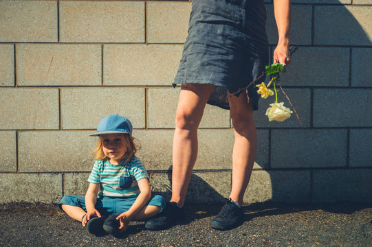 Preschooler sitting on the pavement with his mother standing next to him