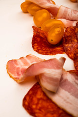 Slices of sausage and bacon and tomatoes on a white background. Close up.