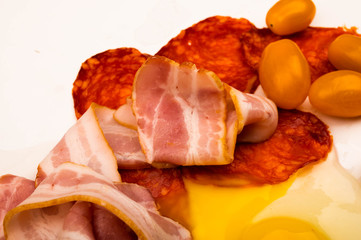 A broken chicken egg without a shell, slices of sausage and bacon and tomatoes on a white background. Close up.