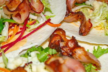 Leafy salad, sliced vegetables, sauce and fried bacon slices on pita bread are the basis for homemade Shawarma. Close up.