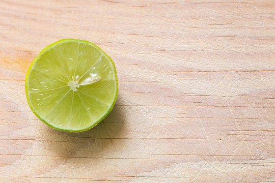 Un lim&oacute;n verde y jugoso cortado en una tabla de madera iluminada con luz natural