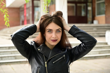 Portrait of a cute young caucasian brunette girl in a black jacket in various poses. Model posing in the city in the spring outdoors.