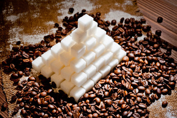 A pyramid made of refined sugar cubes and coffee grains, standing on a dark wooden surface.