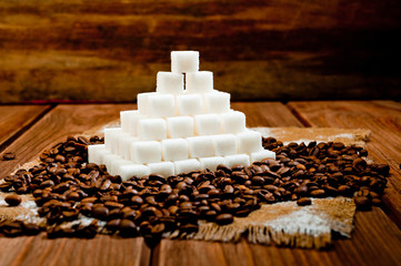 A pyramid made of refined sugar cubes and coffee grains, standing on a dark wooden surface.
