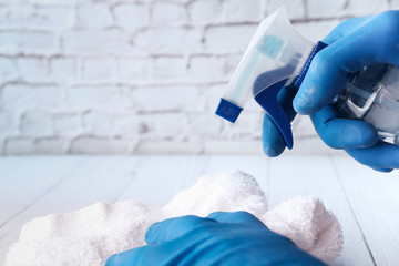 hand in blue rubber gloves holding spray bottle and cleaning table 