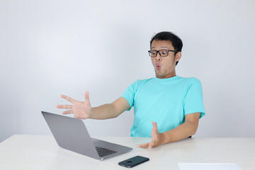 Wow face of Young Asian man shocked what he see in the laptop when working isolated grey background wearing blue shirt.
