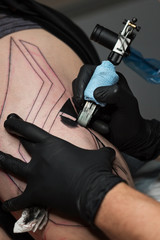 Fototapeta na wymiar Professional tattoo artist makes tattoo on man leg. Process. Introduces black ink into skin using needle from tattoo machine. Close up of tattoo machine. Tattooing. Master creating picture on leg.