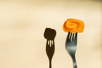 Fork with orange color dumplings on the background of a wall with a shadow