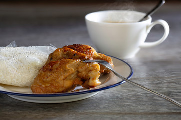Fried chicken with sticky rice in plastic bag on white dish and hot coffee all put on gray wooden table