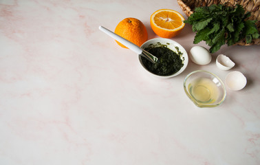 Natural home skin care. Ingredients of a face mask. Crushed nettle leaves, egg white, orange juice and ready-made mask mix in a cup with a spatula on a pastel pink background. Free space.
