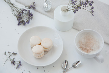 Macarons, morning coffee on light table with blurred vase and blue flowers on background