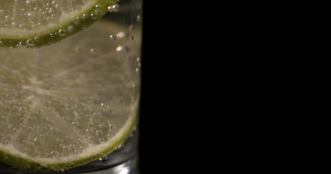 macro sparkling water with lemon and lime with bubbles and ice on a black background. Lemonade in glass 