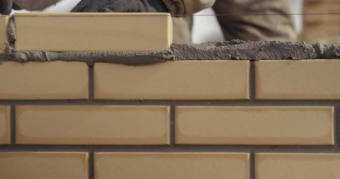 Close-up of new brick wall, streamer finishes laying bricks, professional bricklayer puts last two bricks in row, trowel levels bricks, removes excess mortar, brick still wet, mortar begins to dry out