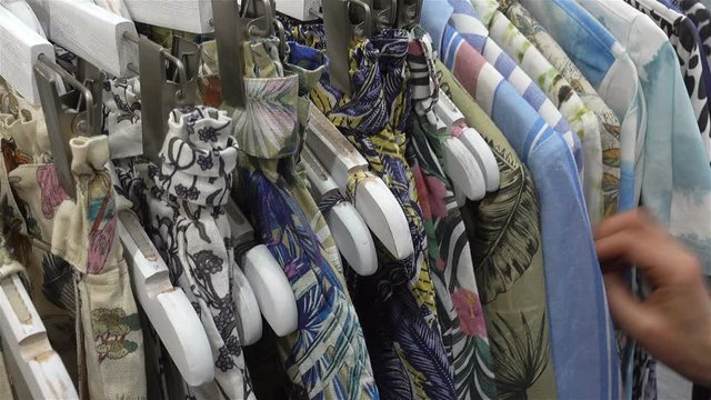 Female hand chooses colorful summer clothes on hangers in a store