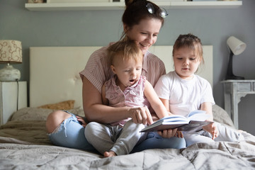 mom is reading book with two children on bed