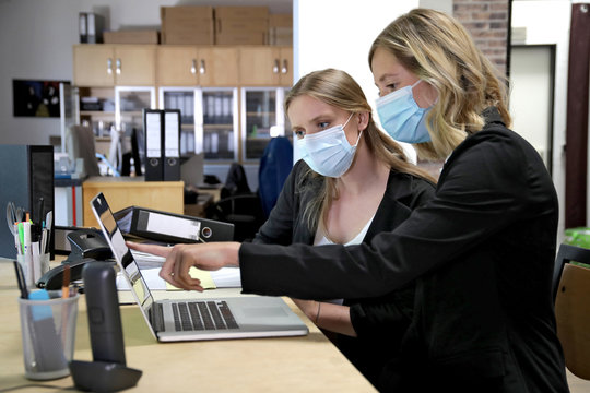 Zwei Büroangestellte mit Mund- und Nasenschutz arbeiten gemeinsam am Schreibtisch