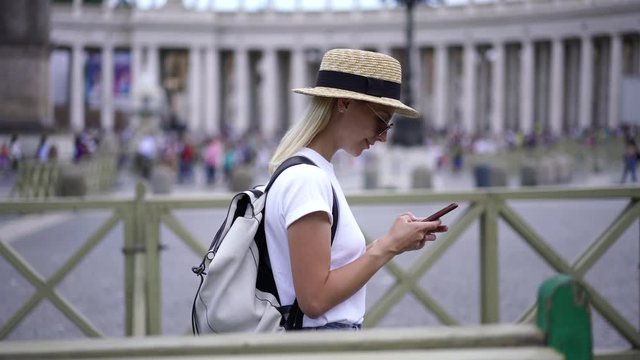 Female travel blogger in casual wear walking during trip and chatting online on smartphone device using pubic 4G internet.Young woman tourist messaging in social networks on cellular

