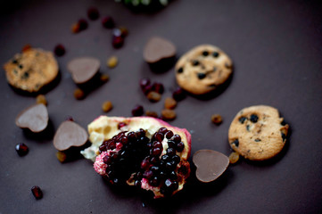 pomegranate, cookies, raisins and chocolate hearts on a dark background. Flat lay. Selective focus.