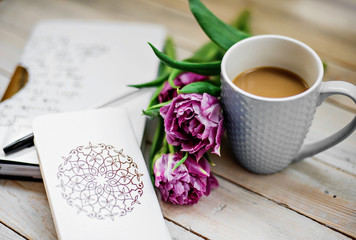 creative arrangement  beautiful dark pink tulips, a notebook, a pen and a cup of coffee on a wooden background. Flat lay. Selective focus.