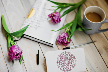 creative arrangement  beautiful dark pink tulips, a notebook, a pen and a cup of coffee on a wooden background. Flat lay. Selective focus.