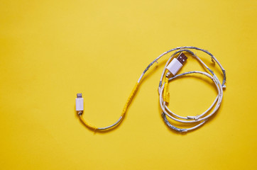 An old torn USB cord is lying on a yellow background. The view from the top.