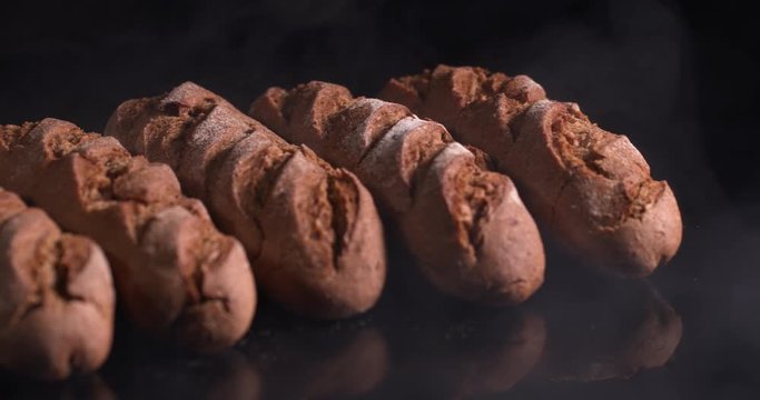 fresh loaf in a row lies on a table in smoke on a black background  