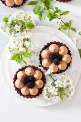 Obraz na płótnie Canvas Chocolate tart with caramel filling and fresh blackberries. Cherry flowers on background. Copy space
