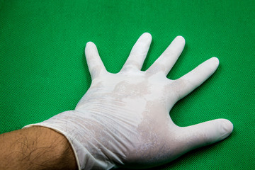 One hand is put on medical gloves placed on a green ground.