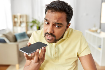 technology, remote job and lifestyle concept - angry indian man using voice command recorder on smartphone at home office