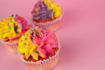 Homemade cupcakes with multi-colored cream on a pink background copy space. Yellow and pink cream. Cupcakes with confetti. Birthday cakes.